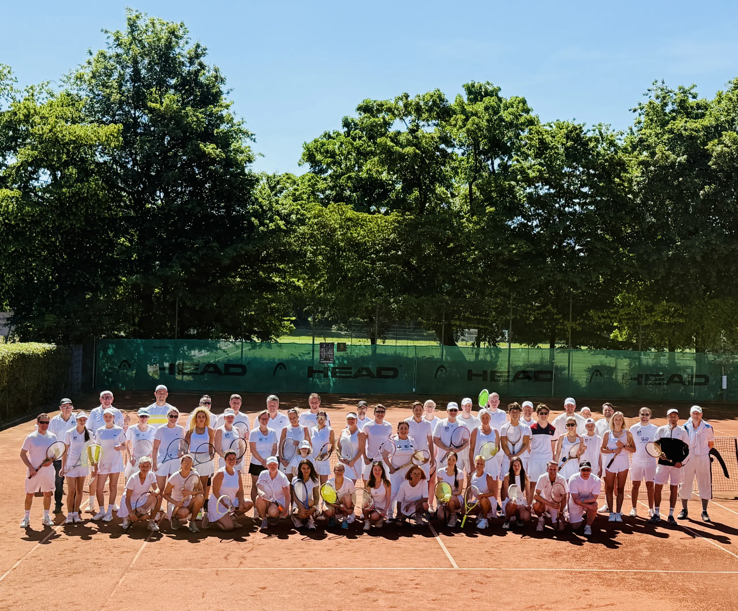 Gruppenfoto der Teilnehmerinnen und Teilnehmer des Pro-Am-Turniers ganz in Weiß auf dem Sandplatz